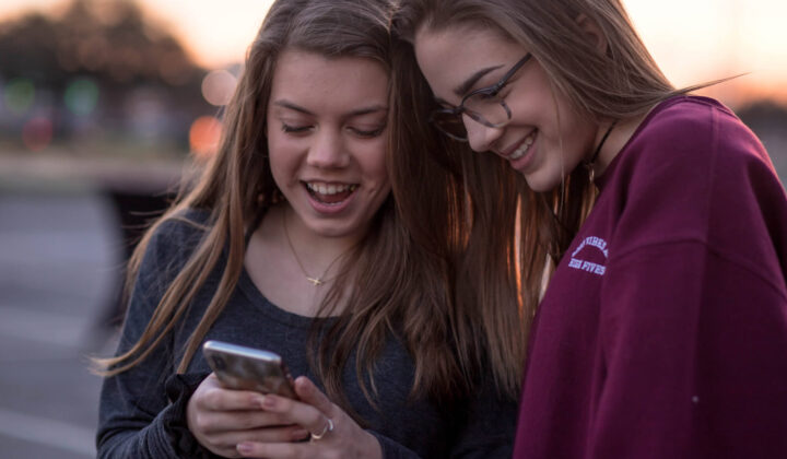 Two young girls smile and look at a mobile phone