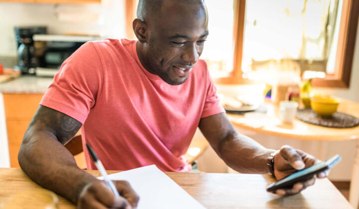 Man writing on paper whilst on his phone