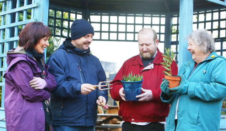 A group of people outdoors holding plants and smiling
