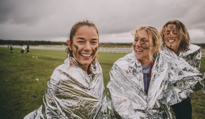 Group of smiling girls in silver blankets after completing a charity mud run