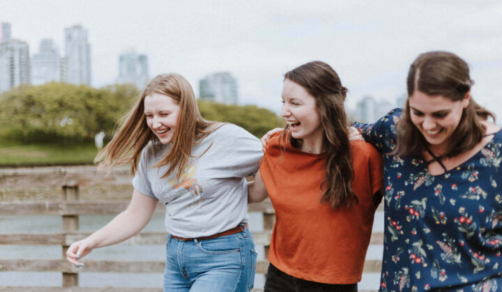 Three young women walking with their arms over each others shoulders smiling