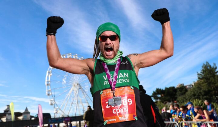 Male charity runner holds arms in the air with mouth open in victory