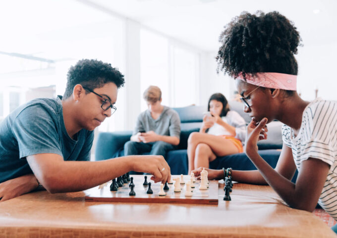 Young friends playing chess and others using smartphone