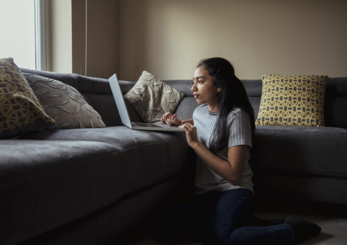 Young girl looking at her laptop sat on the floor