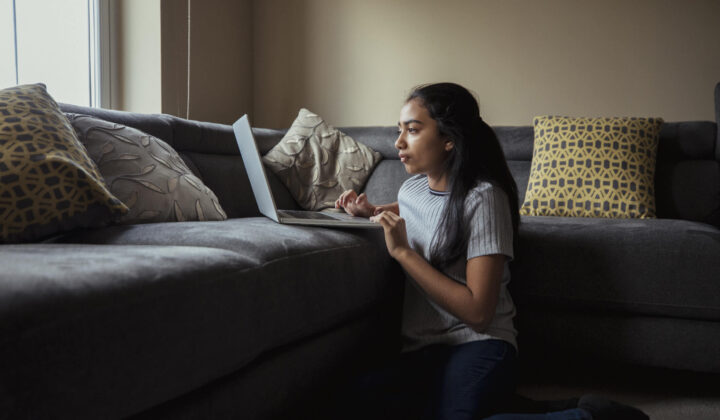 Young girl looking at her laptop sat on the floor