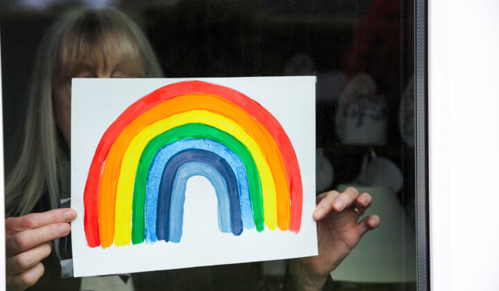 Woman holding rainbow illustration in window - Covid-19