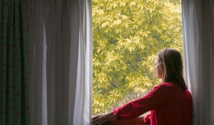 lady looking outside her home at autumn leaves