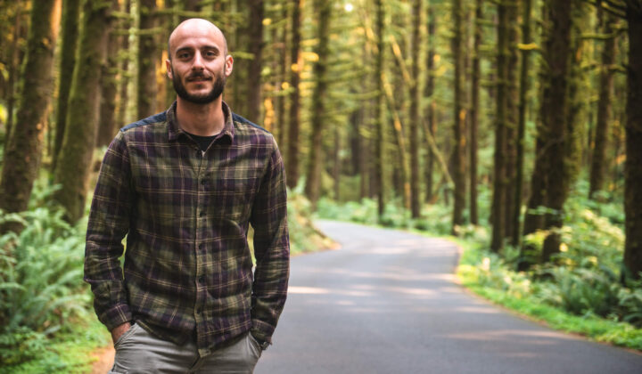 Male standing on a country road in front of woodland trees
