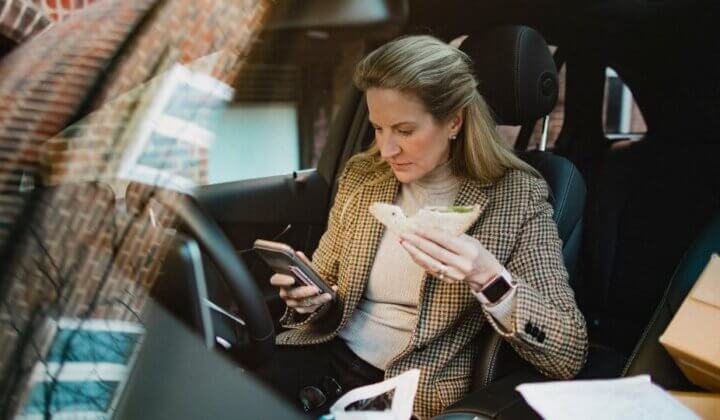 Office worker looking at mobile in parked car whilst eating