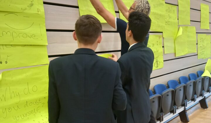Two young people and a facilitator using putting up post-it notes on a wall in mental resilience workshop