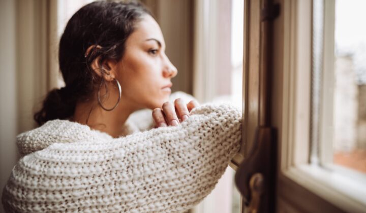 Young women wearing a cream jumper looking sad gazing out of window