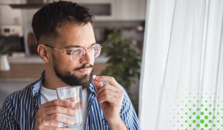 Man looking out of the window taking some medication with a glass of water